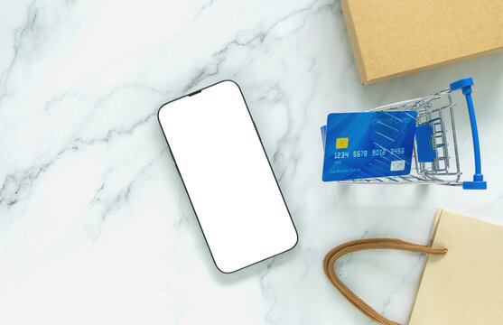 Blank smartphone mockup with credit card, shopping cart and kraft package on white marble, illustrating ecommerce, online shopping, mobile payment, retail, digital commerce and product promotion.