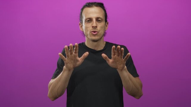 Man with long hair and open palms showing hands in a purple studio wearing black t shirt, facing camera and gesturing with both hands; pleading for help.