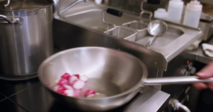 Frying meal. Cooking pan. Chef hand mixing cut garlic radish with boiling bubbling steaming oil in metal skillet on professional stove.