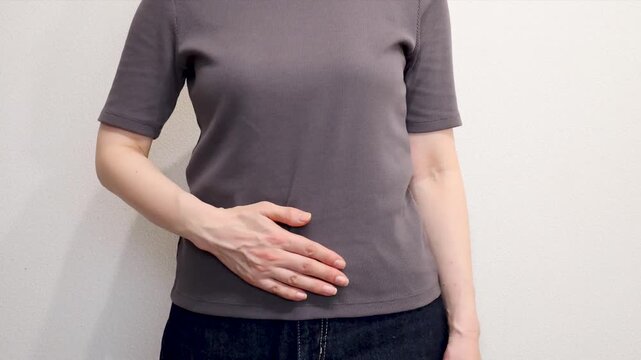 片手で腹部をさする女性の上半身