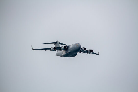 C-17 Globemaster III military transport aircraft photographed in flight against an overcast sky, viewed from below with four jet engines, high-mounted wings.