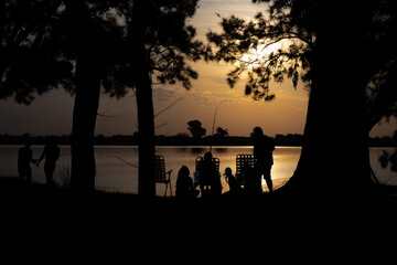 Group of friends silhouetted fishing by the lake at sunset © Jose Ferreyra