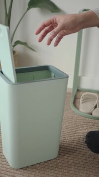 woman disposes of a plastic medicine bottle in a green trash bin at home