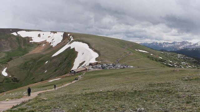 People hiking near mountain parking lot with snow patches.