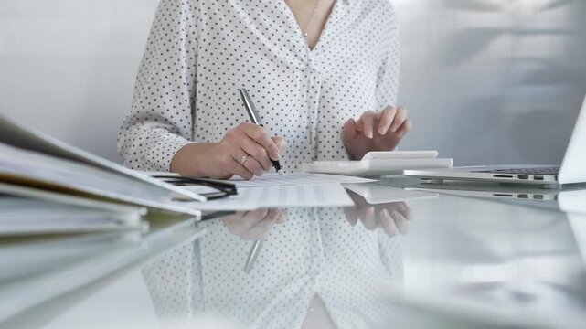 Focused businesswoman at a sleek glass desk in a contemporary office, using a calculator to crunch numbers and jotting down meticulous notes. Taxes, audit in business