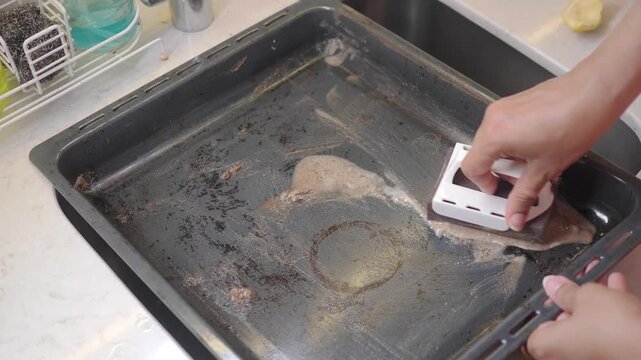 Cleaning a baking tray in the kitchen with a scrubbing tool