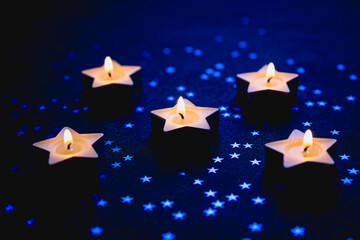 Obraz premium Five lit star-shaped tealight candles glow softly against a dark blue backdrop scattered with small star confetti, creating a warm ambient mood.