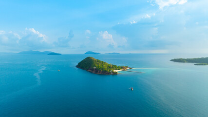 Obraz premium Panoramic aerial view of a lush green tropical island in the middle of a vast blue ocean under a bright sky with clouds, representing vacation, travel, and scenic nature.concept travel