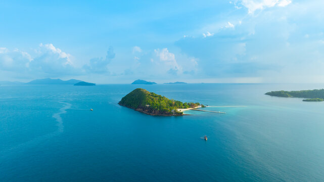 Panoramic aerial view of a lush green tropical island in the middle of a vast blue ocean under a bright sky with clouds, representing vacation, travel, and scenic nature.concept travel