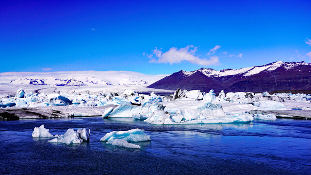 Large clusters of calved icebergs float across J&ouml;kuls&aacute;rl&oacute;n glacial lagoon with snow-capped mountains and the Vatnaj&ouml;kull ice cap stretching across the horizon in southeastern Iceland