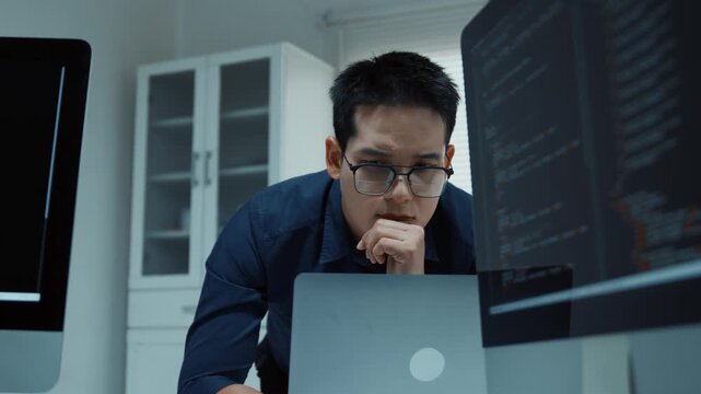 Pensive Asian programmer thinking and debugging code on multiple computers in a modern office at night