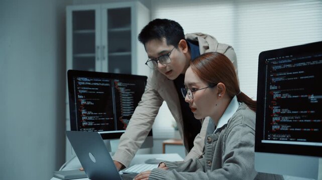 Asian software developers collaborating on programming code and debugging in a modern office at night