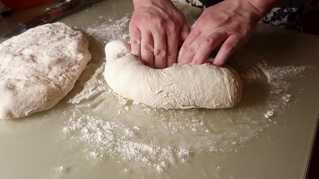 Close-up of hands working a ball of raw dough on a floured surface, showing the process of kneading