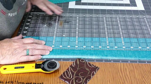 An older woman measuring and cutting a strip of cloth for a quilt.
