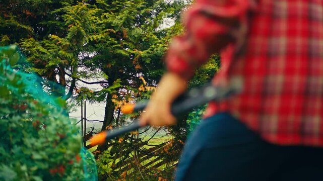 Man uses loppers to cut branches in a garden in rural Norway, showing outdoor gardening and plant maintenance work