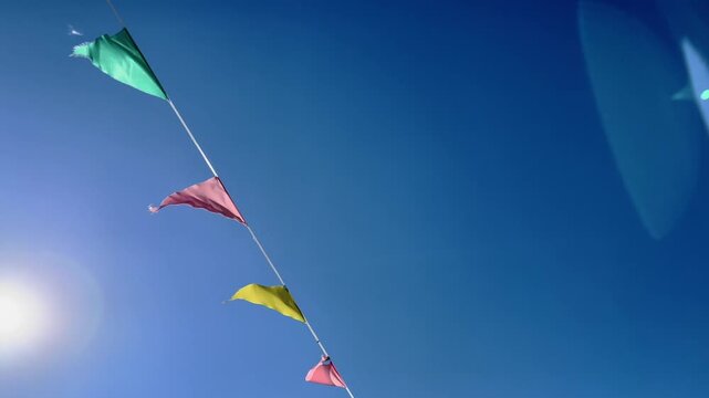 Colorful triangular bunting flags flutter diagonally across a clear blue summer sky