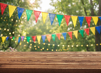 Triangular bunting frames wooden tabletop with colorful celebration decor. Bunting stands against blurred garden greenery and glowing lights, giving festive mood and bright party backdrop appeal. © Agil