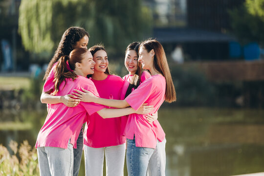 Diverse group of multinational beautiful women wearing stylish pink t shirt with ribbon hugging