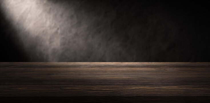Wooden tabletop waits beneath dark wall. Empty surface and moody light create product display space, giving wooden table clean backdrop for packaging, props, or menu layouts with visible wood grain.