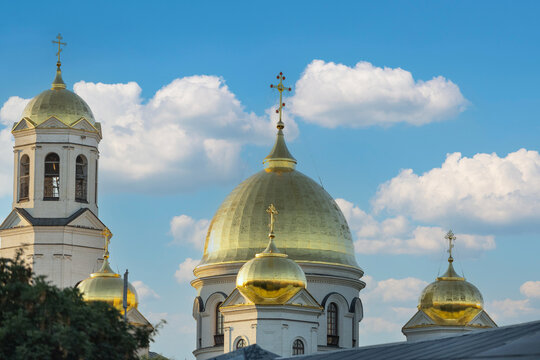 Golden domes crown Orthodox church towers under clear blue sky. White masonry and small arched windows frame sacred architecture, with crosses rising above towers and ornate roof details visible.