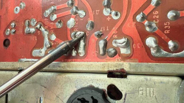 Hot soldering iron tip melts solder on vintage red circuit board during electronics repair