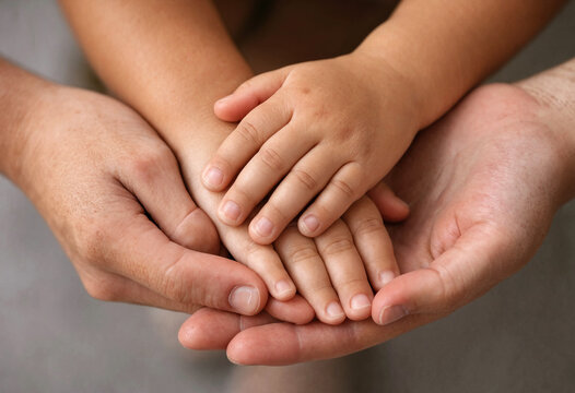 Adult hands gently holding a small childs hands together