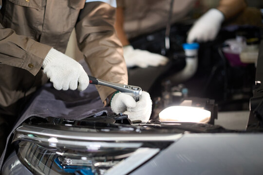 Mechanic hands wearing white gloves using a wrench to fix a car engine