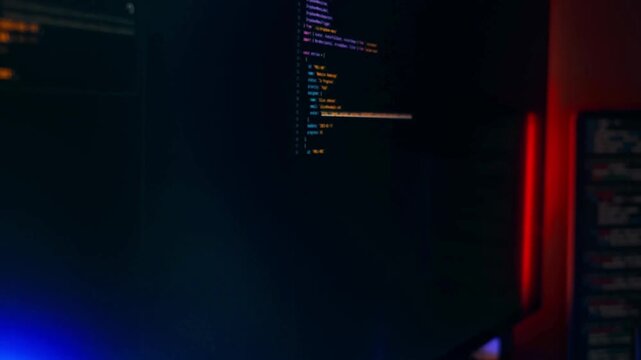 Developer analyzing code on dual monitor setup in dimly lit office with neon lighting accents