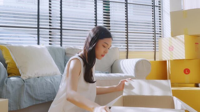 Young Asian woman happy and smiling unpack boxes at new house, relocation and people in real estate or apartment. Moving house concept