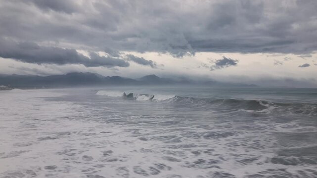 Drone Shot Stormy Sky And Large Waves Breaking Along Tropical Coastline With Mountains In Distance