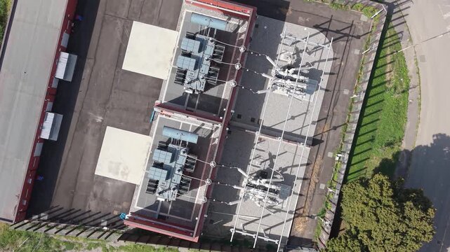 Aerial view of an electrical substation featuring transformers and power equipment within a fenced facility surrounded by trees and vegetation in Lombardy, Italy.