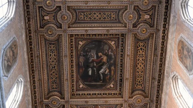 Decorated coffered ceiling in Naples Cathedral centers on a religious painting framed by carved gold details and side frescoes.