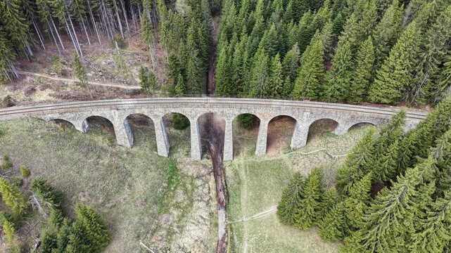 Aerial top down view flying over the historic Chmaroska Viaduct, an arched stone railway bridge crossing a valley in Slovakia