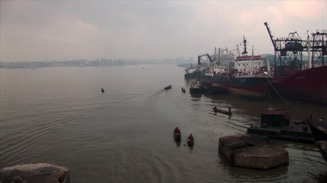 Atmospheric view of an industrial harbor in Lagos, Nigeria, featuring large red cargo ships and small wooden canoes navigating the hazy water.
