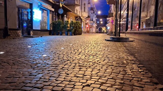 Charming historic cobblestone street at night, illuminated by warm lights from shops and buildings, creating a peaceful urban atmosphere with beautiful architecture and inviting scenery