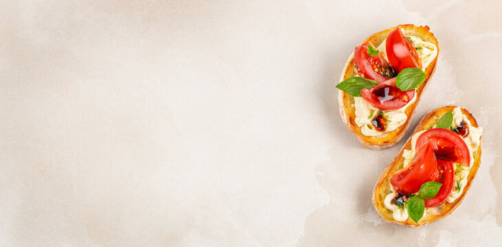 Two slices of toasted bread topped with fresh tomatoes, basil, and creamy cheese on a light textured background, ideal for culinary presentations or food blogs