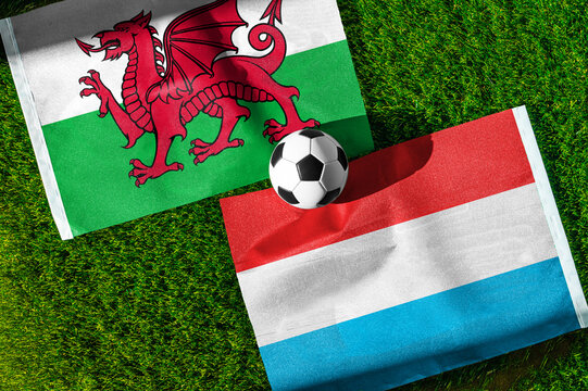 Wales vs. Luxembourg football match. National flags on green grass with soccer ball in the middle. Football background for international match.