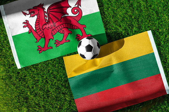 Wales vs. Lithuania football match. National flags on green grass with soccer ball in the middle. Football background for international match.
