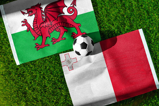 Wales vs. Malta football match. National flags on green grass with soccer ball in the middle. Football background for international match.