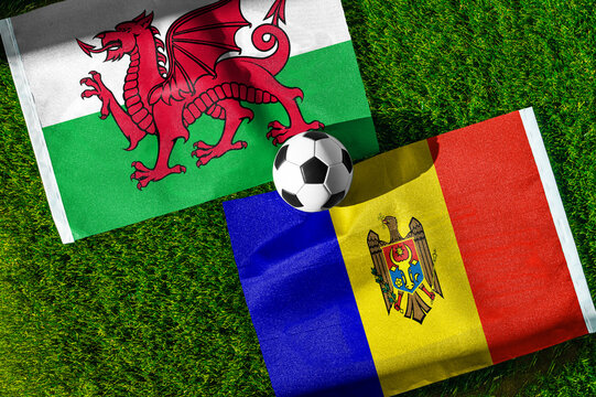 Wales vs. Moldova football match. National flags on green grass with soccer ball in the middle. Football background for international match.