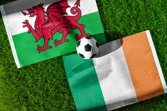 Wales vs. Republic of Ireland football match. National flags on green grass with soccer ball in the middle. Football background for international match.