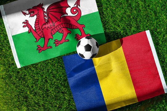 Wales vs. Romania football match. National flags on green grass with soccer ball in the middle. Football background for international match.