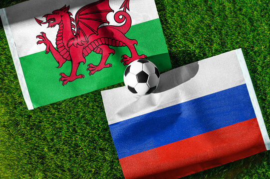 Wales vs. Russia football match. National flags on green grass with soccer ball in the middle. Football background for international match.