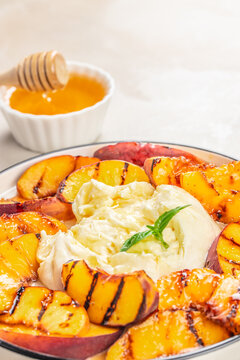 Grilled peaches served with creamy burrata cheese and honey in a white bowl, garnished with fresh mint leaves on a light background