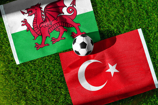 Wales vs. Turkey football match. National flags on green grass with soccer ball in the middle. Football background for international match.