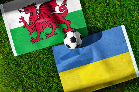 Wales vs. Ukraine football match. National flags on green grass with soccer ball in the middle. Football background for international match.