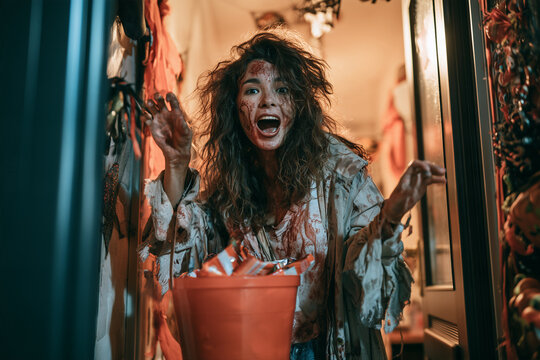 Zombie on Halloween Night Featuring Undead Woman Handing Out Candy from Bucket at Decorated Halloween Doorway