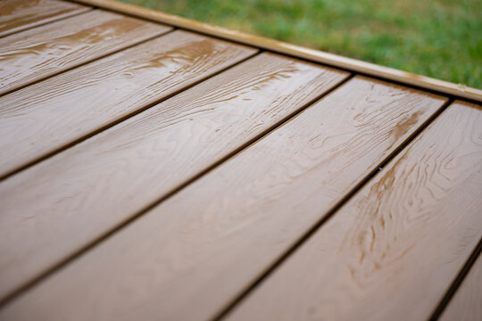 Close-up of wet brown WPC composite decking after rain, showing realistic wood grain, water reflections and modern weather-resistant outdoor terrace flooring.