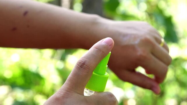 Close up of person spraying insect mosquito repellent on arm for bug bite protection outdoors
