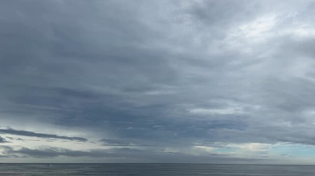 灰色の雲の隙間から柔らかな光が差し込む曇天の海の景色